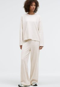 Beige knit sweatshirt with a crew neckline, paired with matching wide-leg pants. Smooth texture and relaxed fit. Casual ensemble.