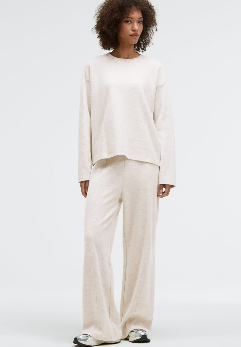 Beige knit sweatshirt with a crew neckline, paired with matching wide-leg pants. Smooth texture and relaxed fit. Casual ensemble.