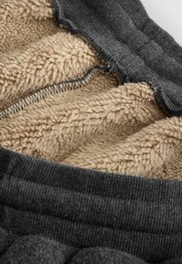 Gråt fleeceforet produkt med en blød tan sherpa indvendig. Har et struktureret ydermateriale og synlig lynlåsdetalje langs sømmen.