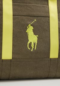 Brun canvasväska med klara gula remmar och en framträdande gul broderad polo spelare-logotyp. Hållbar och strukturerad design.