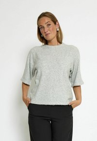 Light gray, short-sleeve sweater with a soft, textured finish and round neckline, paired with black pants. Simple and modern design.