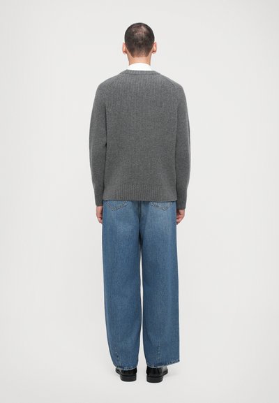 Pull en tricot gris à col rond, associé à un jean en denim bleu ample. Le tissu a une texture côtelée, et le jean comporte des poches arrière.