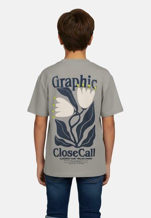 Jongen draagt een grijs T-shirt met een grote afbeelding van witte bloemen en donkere bladeren, tekst op de achterkant luidt "Graphic CloseCall".