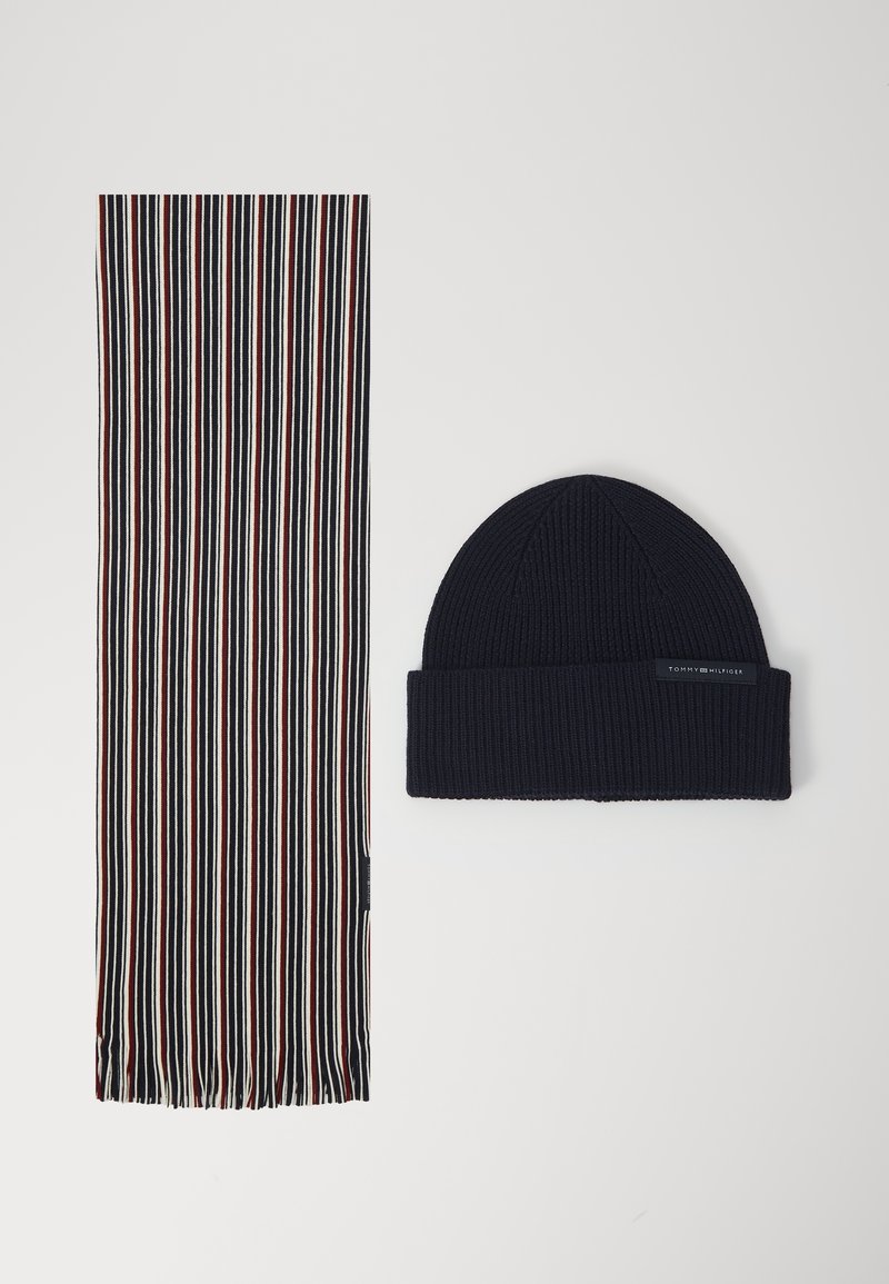 Bonnet en tricot bleu marine avec revers et foulard étroit rayé en bleu marine, blanc et rouge, posé à plat sur fond blanc.
