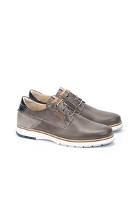 Chaussures en cuir marron avec un design perforé, semelle blanche et talon noir contrastant. Présente des lacets et un petit logo orange.