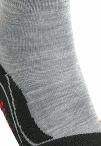 Calcetín gris con secciones de talón y punta negras. El material parece ser de punto, con un acabado texturizado y un detalle de logotipo rojo bordado.