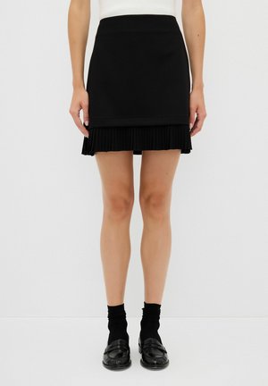 Jupe noire avec un ourlet inférieur plissé, design supérieur élégant et texture de tissu lisse. Associée à des chaussettes noires et à des mocassins.