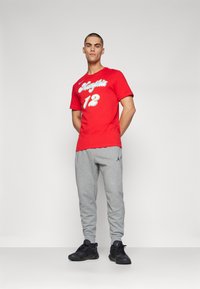 T-shirt rouge avec "Memphis" et "12" imprimés en blanc, associé à un pantalon de jogging gris avec le logo noir de Jordan, et des chaussures de sport noires.