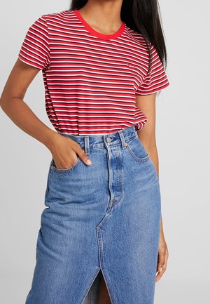 Femme portant un T-shirt rayé rouge, blanc et marine, rentré dans une jupe en jean bleu taille haute avec une fente à l'avant et la main dans la poche.