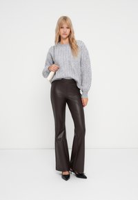 Un pull gris en tricot avec un motif texturé, associé à un pantalon évasé en cuir synthétique marron. Inclut des chaussures noires à bout pointu et un petit sac.