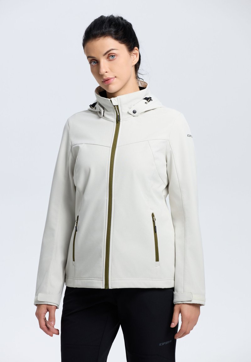 Lys beige softshell-jakke med hætte, grøn lynlås og sidelommer. Har et strømlinet design og en glat tekstur.