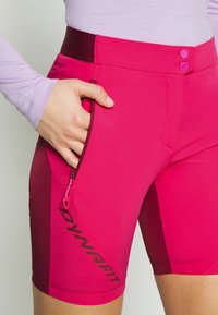Magenta urheilushortsit, joissa on istuva malli, edessä vetoketjullinen tasku ja kontrastivärinen vyötärönauha. "DYNAFIT"-logo on näkyvissä.