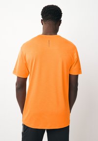 Maglietta sportiva arancione a maniche corte con motivo a trama, scollo rotondo e un piccolo dettaglio verticale di cucitura sul retro.