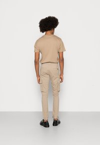 Beige bomulls T-shirt med korta ärmar; kombinerad med beige cargobyxor som har sidofickor och elastiska muddar; svarta platta skor.