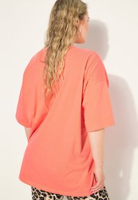 Camiseta coral de gran tamaño con mangas cortas, textura suave, cuello redondo y dobladillo recto. Combinada con leggings de estampado animal.