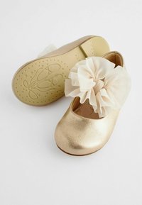Guldmetalliska ballerina-skor med rund tå, prydda med en stor ljuskrämfärgad tyllblomma. Strukturerad sula med ballerina-design.