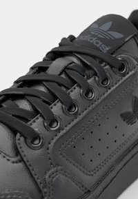 Svart lädersneaker med slät yta, runda svarta snören, perforerade sidor och en präglad logotyp på tungan.