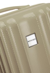 Maleta rígida en beige claro con textura de panal. Presenta un logo de marca plateado y un diseño aerodinámico con sutiles surcos.