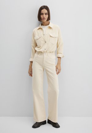 Cremefarbenes Cord-Hemd mit Klappentaschen, gesteckt in passende Hosen mit weitem Bein. Schwarze Stiefeletten runden das Outfit ab.
