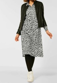 Abito con stampa animale in bianco e nero, con vita aderente e maniche lunghe, abbinato a un giubbotto di pelle nera e sneakers alte bianche.