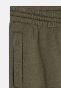 Pantaloni de trening verde măsliniu cu o textură moale, talie elastică și detalii cu buzunare laterale. Materialul pare elastic și confortabil.