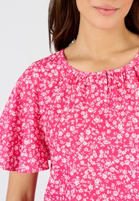 Blusa floreale rosa con maniche a sbuffo corte, scollo arricciato e una stoffa testurizzata con piccoli motivi di fiori bianchi.