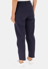 Pantaloni blu navy con vita elasticizzata, tasche posteriori, gambe affusolate e superficie liscia, abbinati a sneaker bianche.