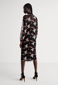 Vestido florido preto com mangas longas transparentes, apresentando padrões de flores coloridas. Silhueta ajustada com comprimento até a metade da panturrilha.