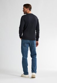 Dunkelblauer Pullover aus weichem Material, taillierte Passform, lange Ärmel, kombiniert mit hellblauen Jeans und weißen Sneakers.