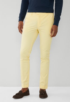 Pantalones chinos de color amarillo claro con un ajuste slim, que presentan bolsillos frontales y una textura suave, combinados con mocasines marrones oscuros.