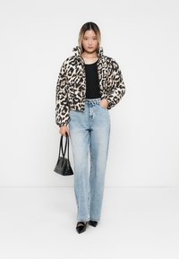 Kort pufferjack in luipaardprint, met een hoge kraag, zachte textuur en knoopsluiting. Gecombineerd met lichtgewassen jeans en een zwarte tas.