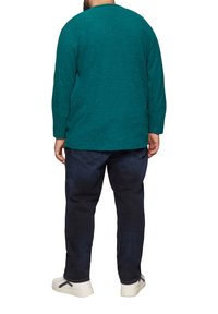 Türkisen Langarmshirt mit gepunktetem Muster, kombiniert mit dunkelblauen Jeans und weißen Sneakers, von hinten betrachtet.