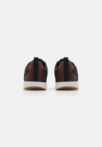 Black sneakers with brown leather accents, white rubber soles, and textured mesh material. Features a pull tab at the heel for easy wear.