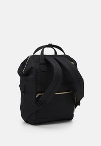 Sac à dos en tissu noir avec accents de fermeture éclair dorés, doté de bretelles réglables, d'une poche avant et d'un design structuré. Surface texturée.