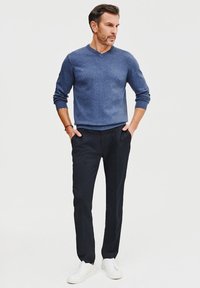Granatowy sweter z dzianiny z dekoltem w serek, zestawiony z czarnymi spodniami od garnituru i białymi trampkami. Sweter ma prążkowane mankiety i dół.
