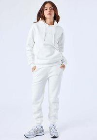 Completo con felpa con cappuccio e pantaloni della tuta in morbido tessuto. La felpa presenta un cappuccio con cordini e una tasca frontale; i pantaloni hanno polsini a coste con dettaglio del logo.