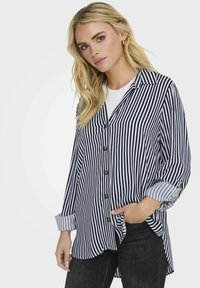 Camisa de rayas en azul marino y blanco de manga larga con un corte relajado, que cuenta con un cuello con solapa, cierre de botones en el frente y un dobladillo curvado.
