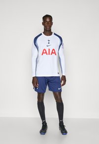 Maglietta da calcio bianca a maniche lunghe con dettagli blu navy, dotata di un logo e del testo rosso "AIA". Abbinata a pantaloni corti blu navy e calzini e scarpe nere.