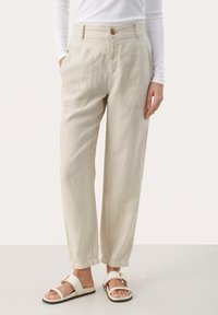 Light beige linen pants with a relaxed fit, featuring side pockets, a button closure, and elastic cuffs, paired with cream-colored sandals.