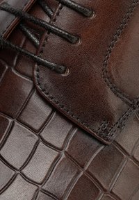 Hnědá kožená společenská obuv se vzorem krokodýlí kůže, černými tkaničkami a detailním prošitím na svršku.