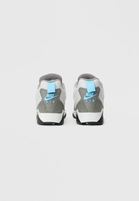 Sapatos Nike Air com um design em cinza e branco, detalhes em azul e uma sola de borracha texturizada. Apresentam um colarinho almofadado e uma aba do calcanhar em contraste.