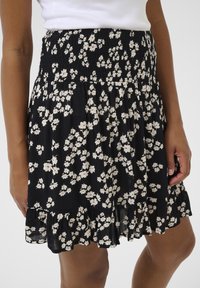 Falda negra con flores blancas y rojas, cinturilla fruncida, dobladillo con volantes y tejido ligero. Termina por encima de la rodilla.