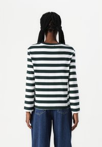 Maglietta a maniche lunghe con righe verdi e bianche, realizzata in tessuto morbido. Collo rotondo e vestibilità rilassata con cuciture visibili all'orlo.