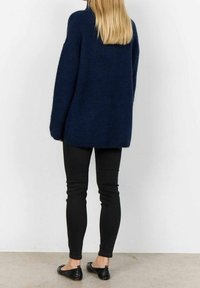 Pull surdimensionné bleu marine en tissu duveteux avec encolure ronde et épaules tombantes, associé à un jean skinny noir et des ballerines noires.