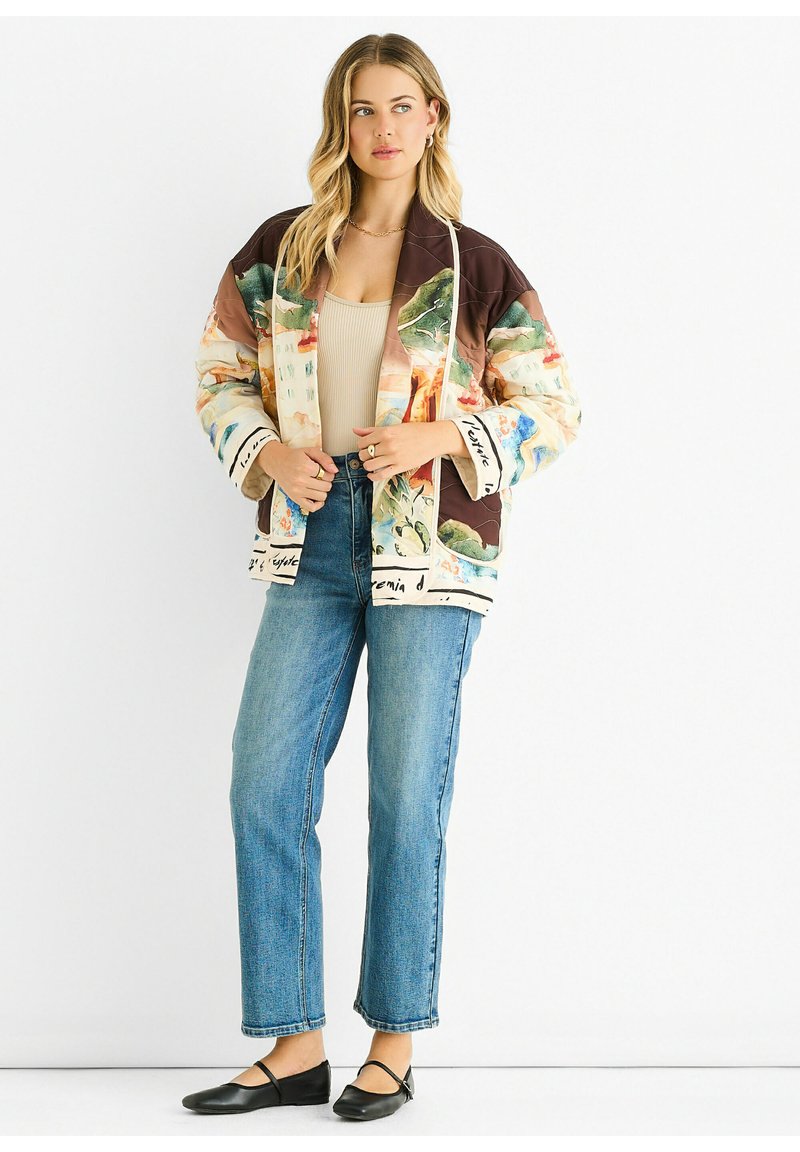 Multicolored quilted bomber jacket with a mix of painted landscapes, brown sleeves, and contrasting cuffs with text. Classic jeans and flats.
