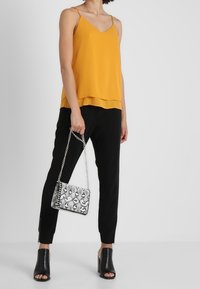 Žluté saténové tílko s vrstveným okrajem, černé kalhoty na míru, texturovaná černobílá kabelka s hadím potiskem a černé sandály na blokovém podpatku s otevřenou špičkou.