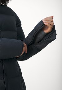 Prošívaná bunda tmavě modré barvy s manžetou na zip. Materiál je hladký a izolovaný, s žebrovanou vnitřní podšívkou.