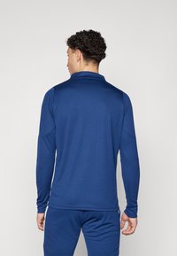 Maglietta atletica a maniche lunghe di colore blu scuro, realizzata in tessuto testurizzato con colletto. La parte posteriore presenta un design pulito e minimalista senza grafica.