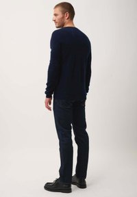 Marineblauer Strickpullover mit lockerer Passform, langen Ärmeln und runder Ausschnitt, kombiniert mit dunklen Jeans und schwarzen Schuhen.