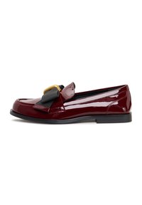 Mocassin en cuir verni bordeaux avec un accent de ruban noir et des garnitures dorées. Semelle plate et texture lisse, avec un design à bout arrondi.